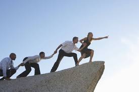 Un grupo de personas se ayuda mutuamente a subir por una roca escarpada, simbolizando el apoyo del Coaching Social para salir del bucle y avanzar colectivamente.